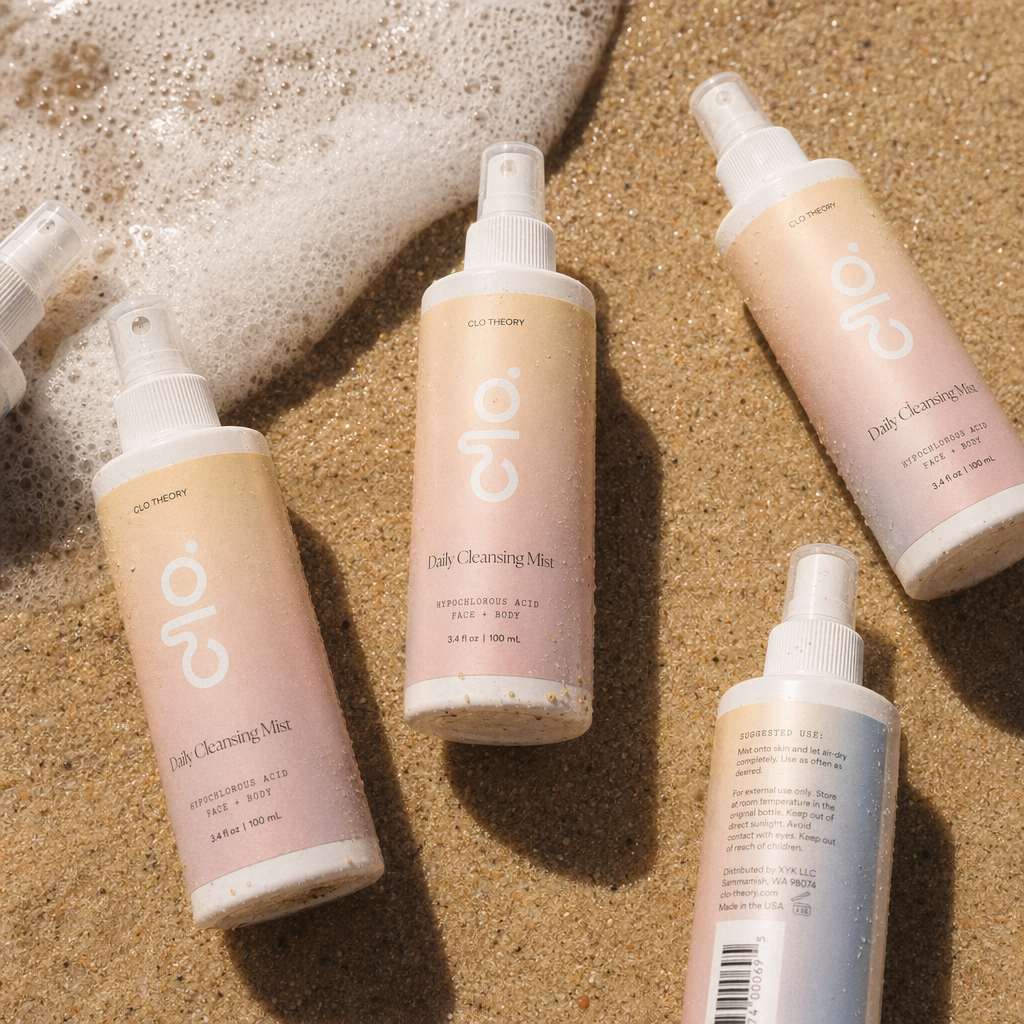 CLO Daily Cleansing Mist bottles on warm sand beside sea foam